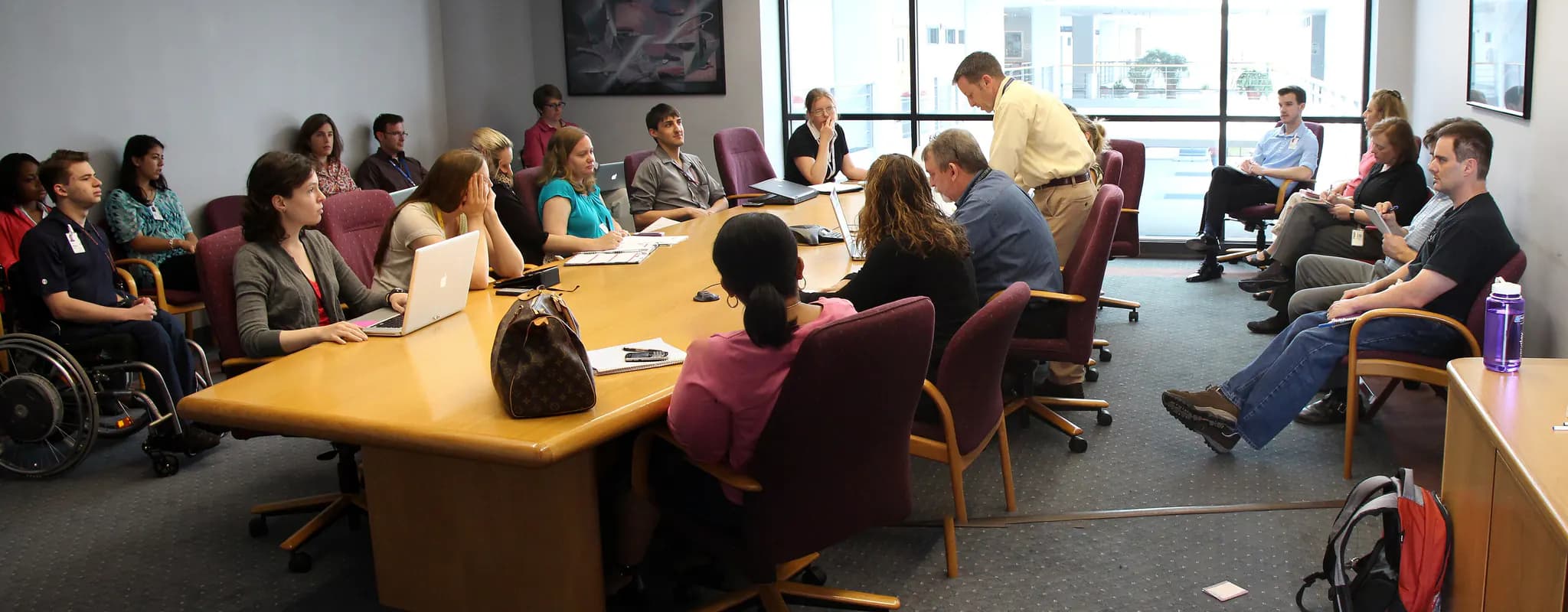 A diverse group of colleagues gathers around a large table for an office meeting.