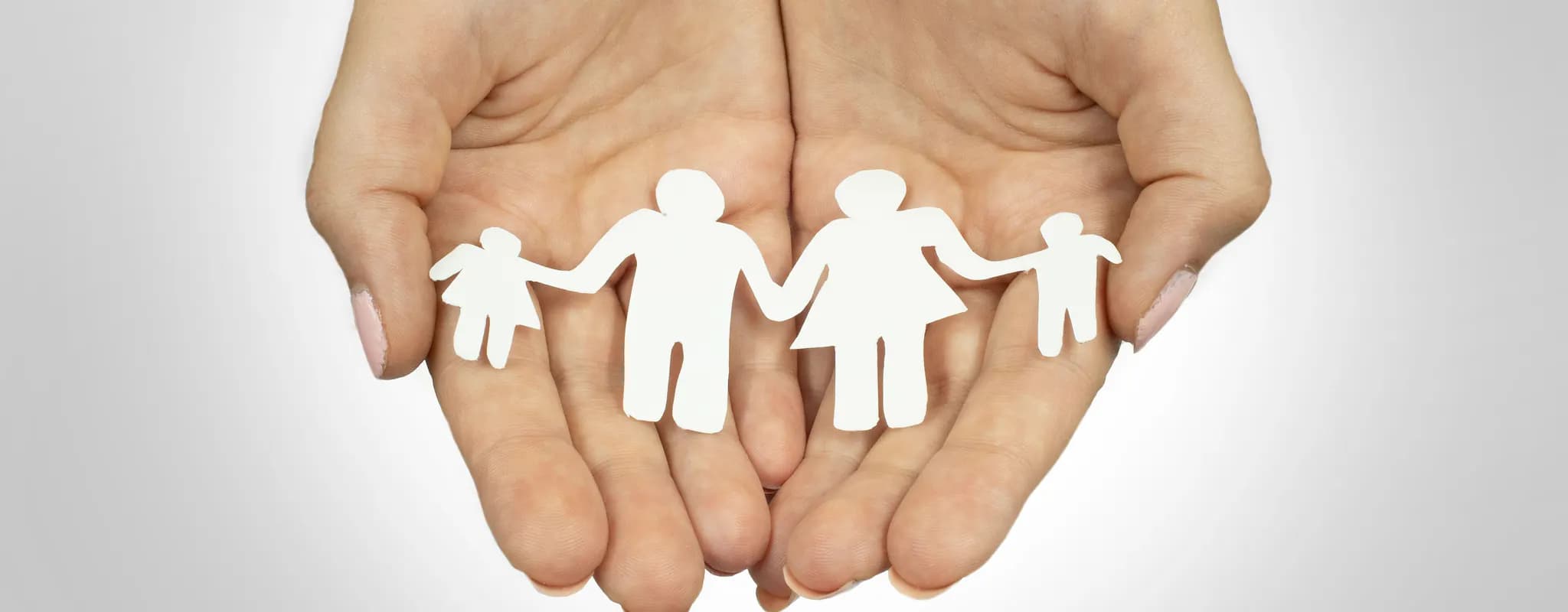 Two open hands hold a white paper cutout of two adults and two children.