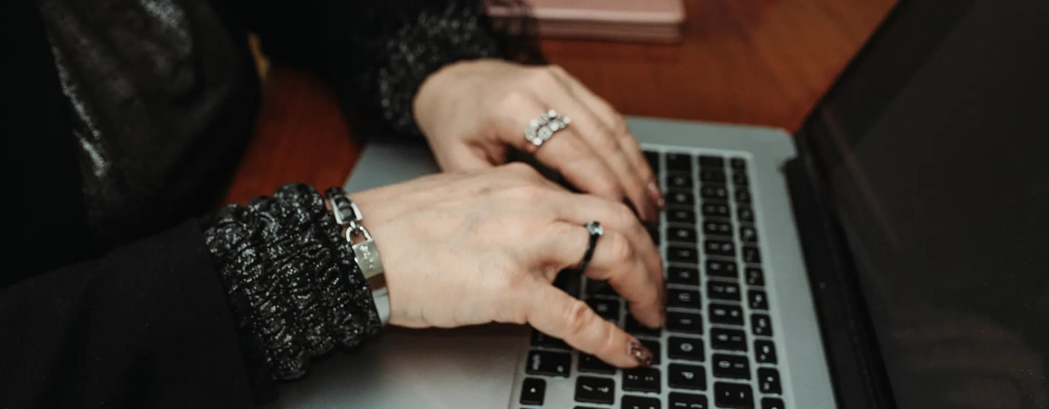 Hands enter information on a laptop at a wooden desk.