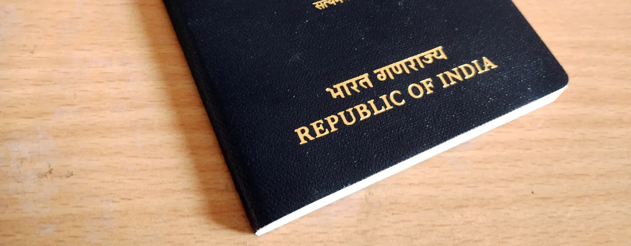 A closed Indian passport rests on a wooden table.