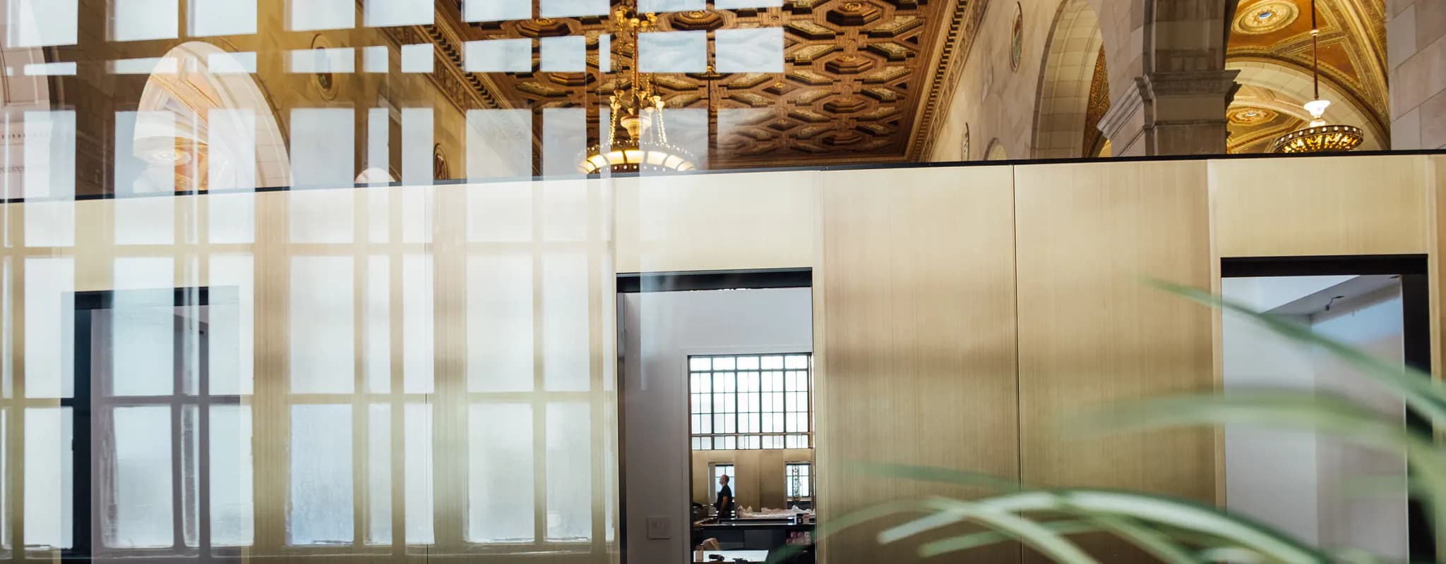 A professional works on a laptop in a modern open office framed by glass reflections.