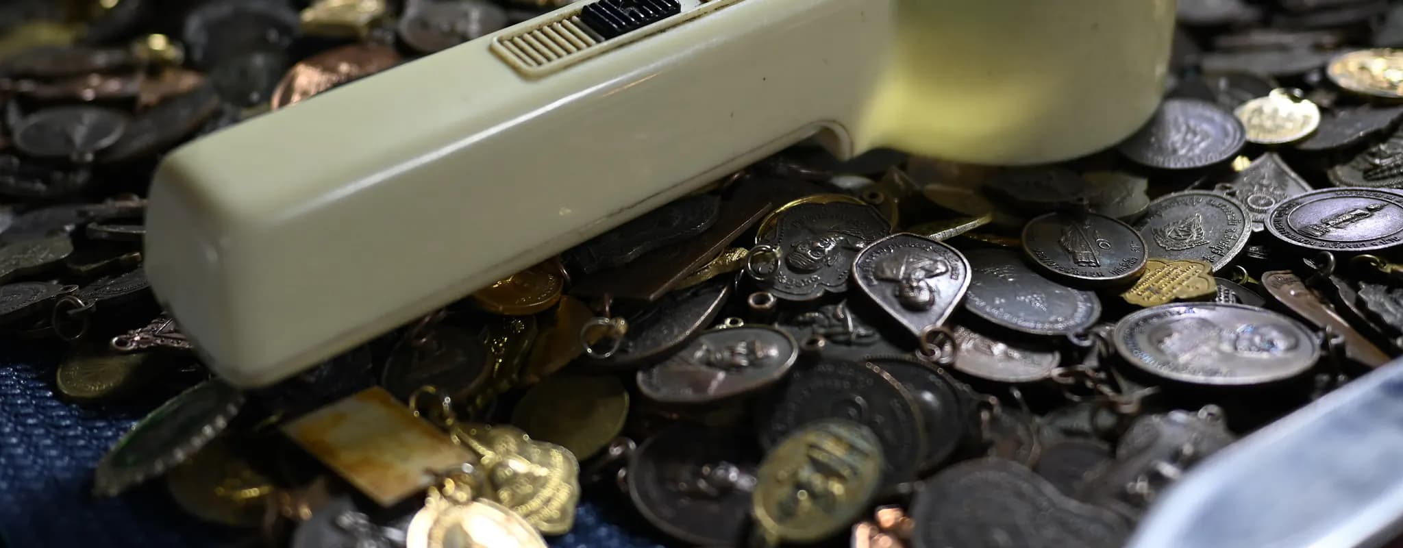 A handheld magnifying glass rests across a tray of assorted coins and medallions.