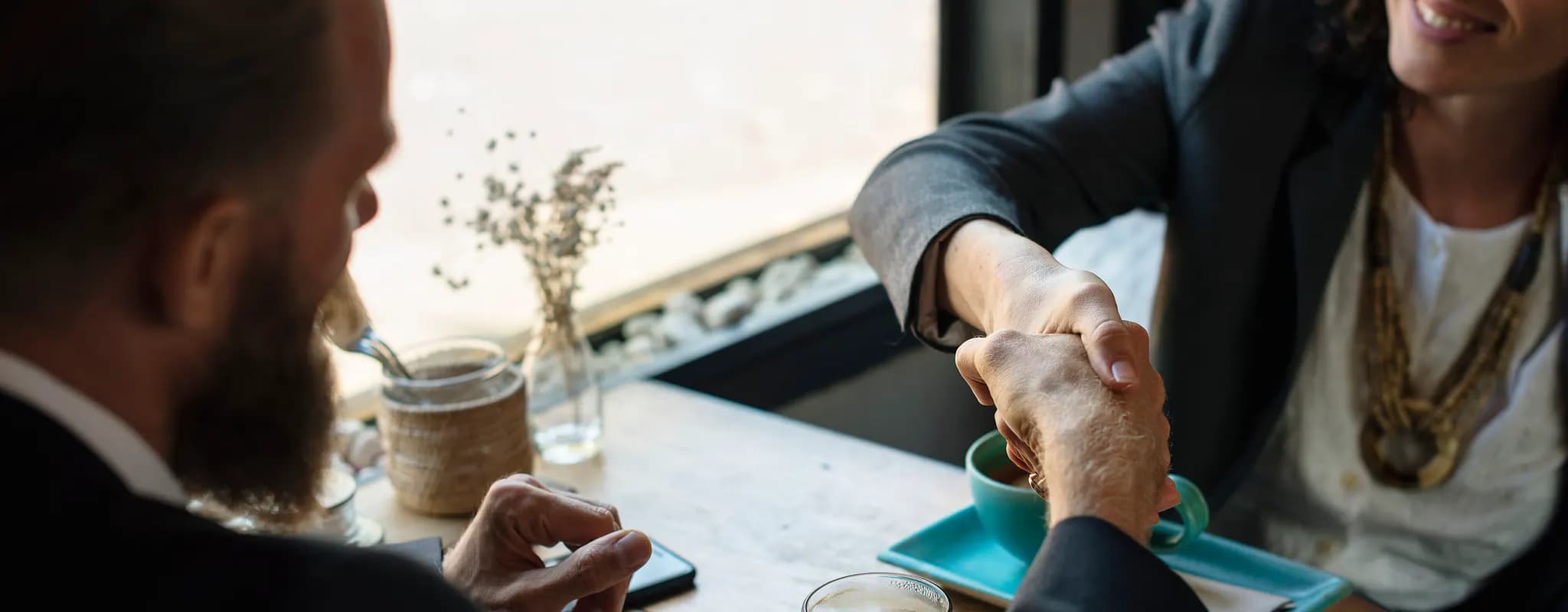 Two businesspeople shake hands across a café table.