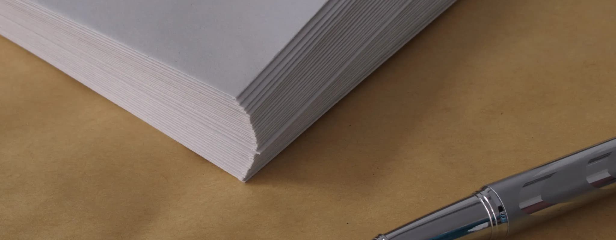 A silver pen lies beside a neat stack of office envelopes.