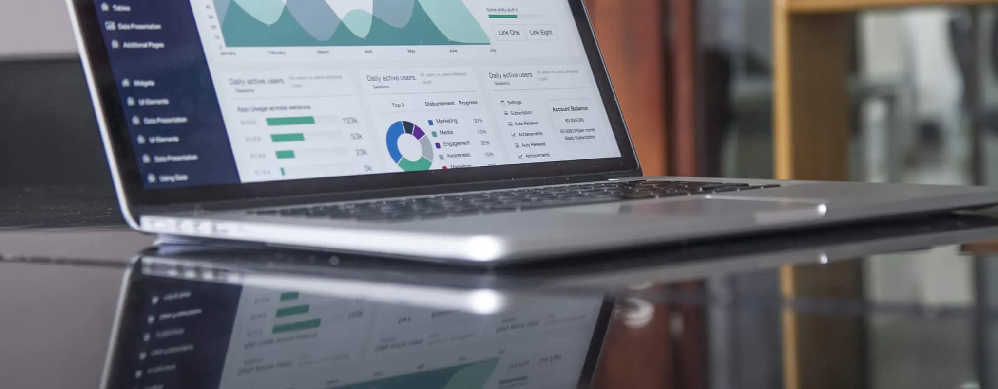 A laptop displays a dashboard of charts and performance statistics on a reflective table.