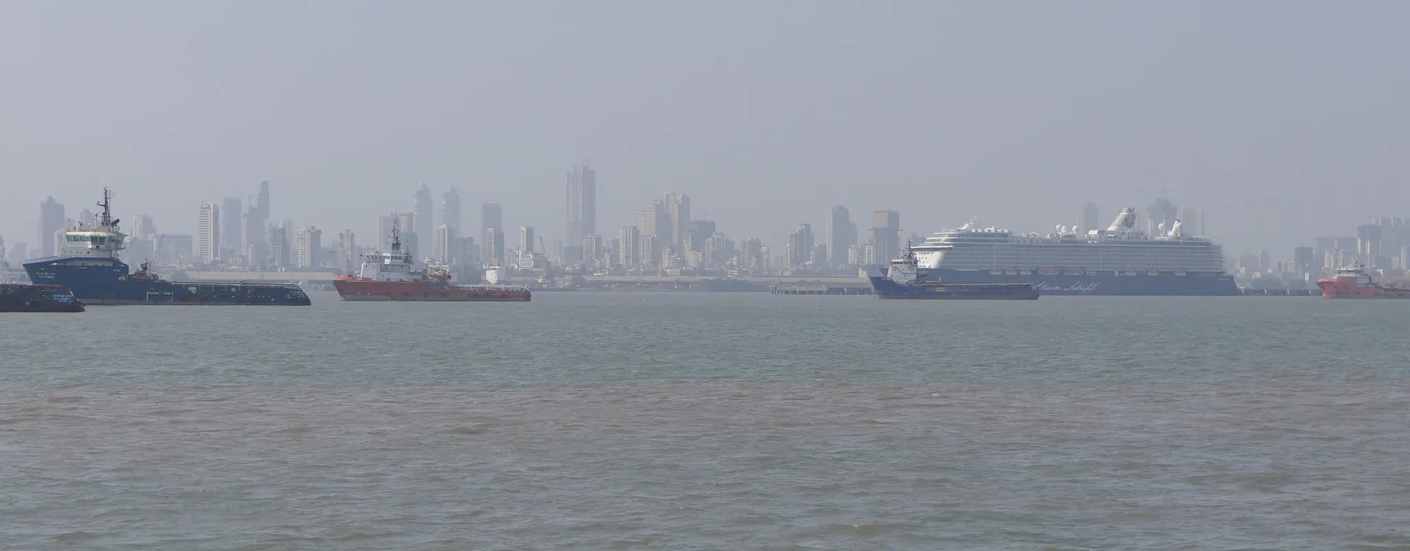 The Mumbai skyline across the harbour with commercial vessels in the foreground.