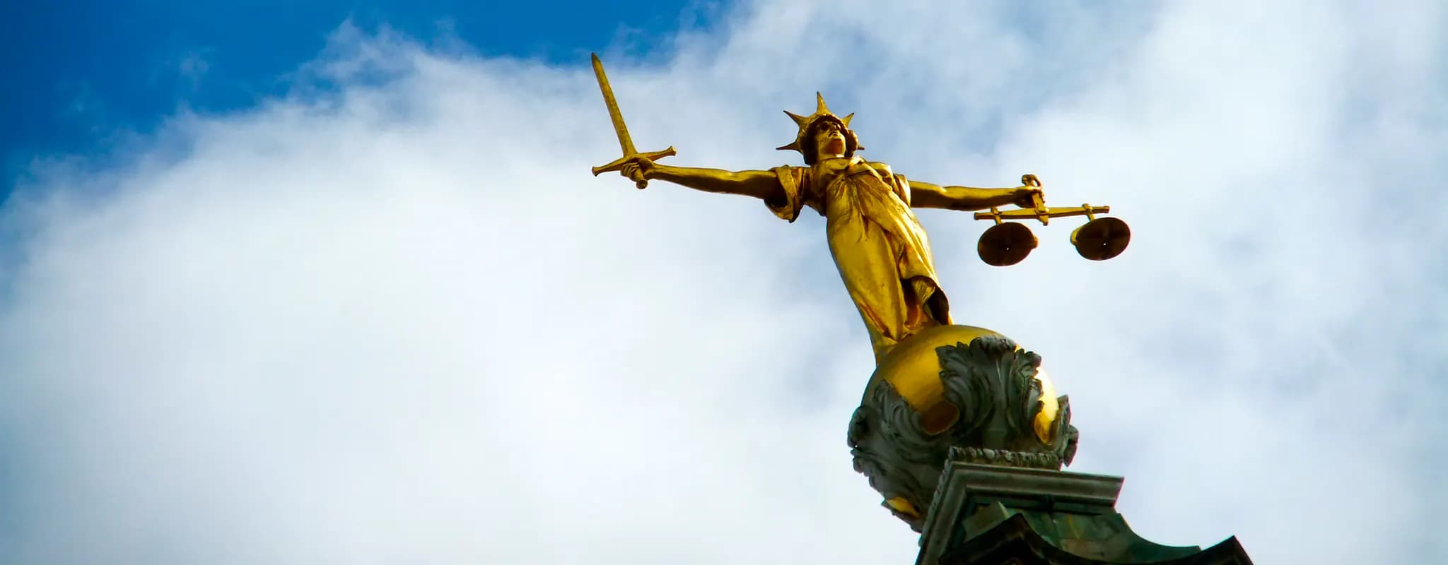 A golden Lady Justice statue holds a sword and balance scales against the sky.