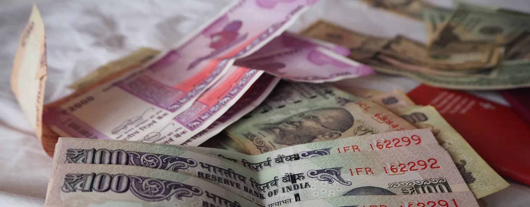 Indian rupee banknotes lie in a shallow stack, with ₹100 notes in the foreground.