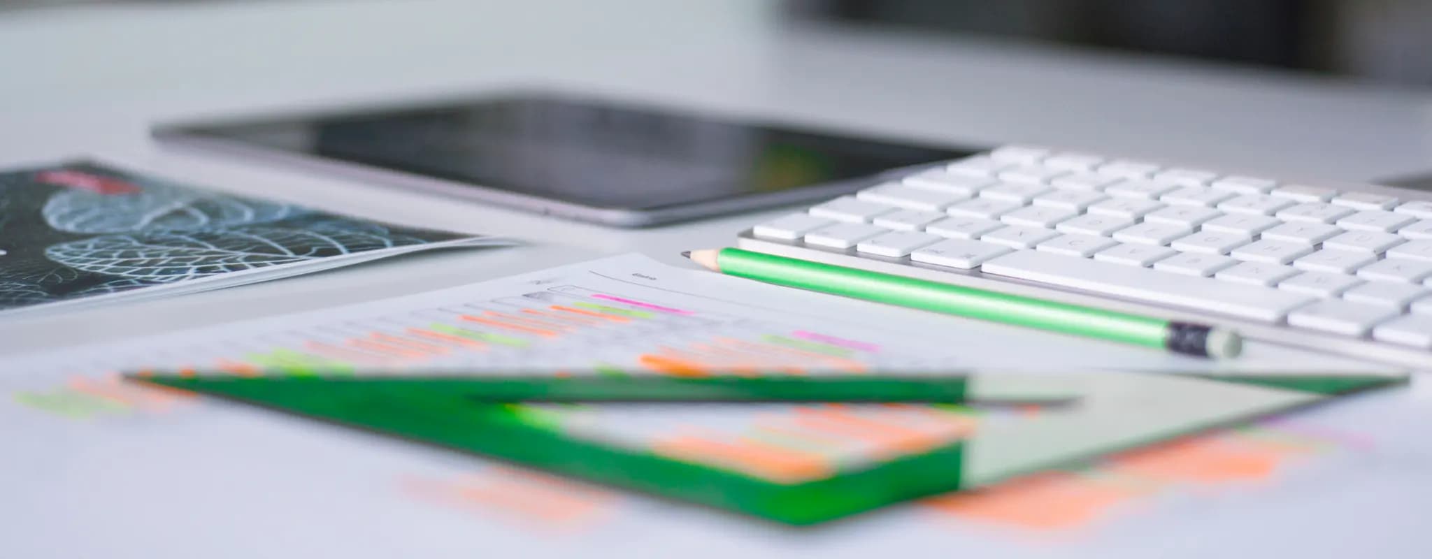 A tidy office desk holds a keyboard, tablet, pencils and neatly arranged working papers.