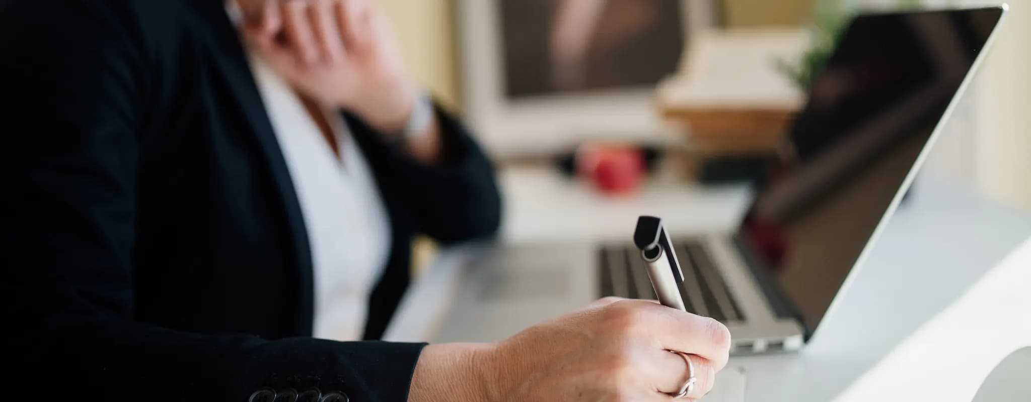 A business professional takes notes beside a laptop during a meeting.