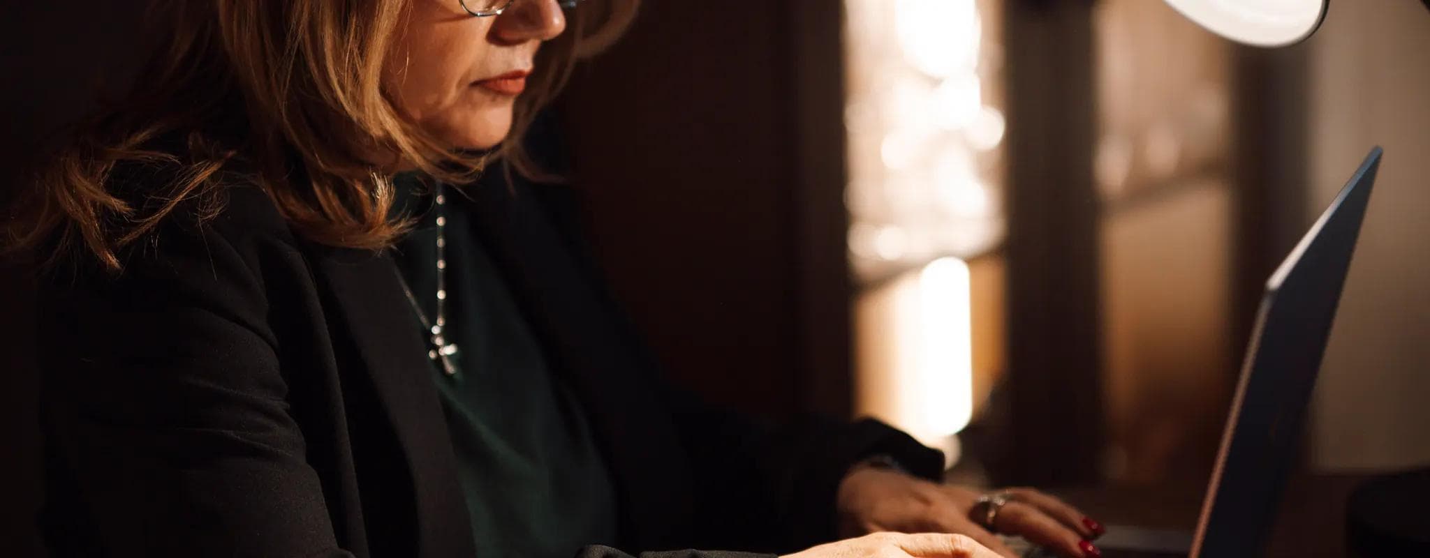 A businesswoman works on a laptop at a desk with an open notebook and coffee mug.