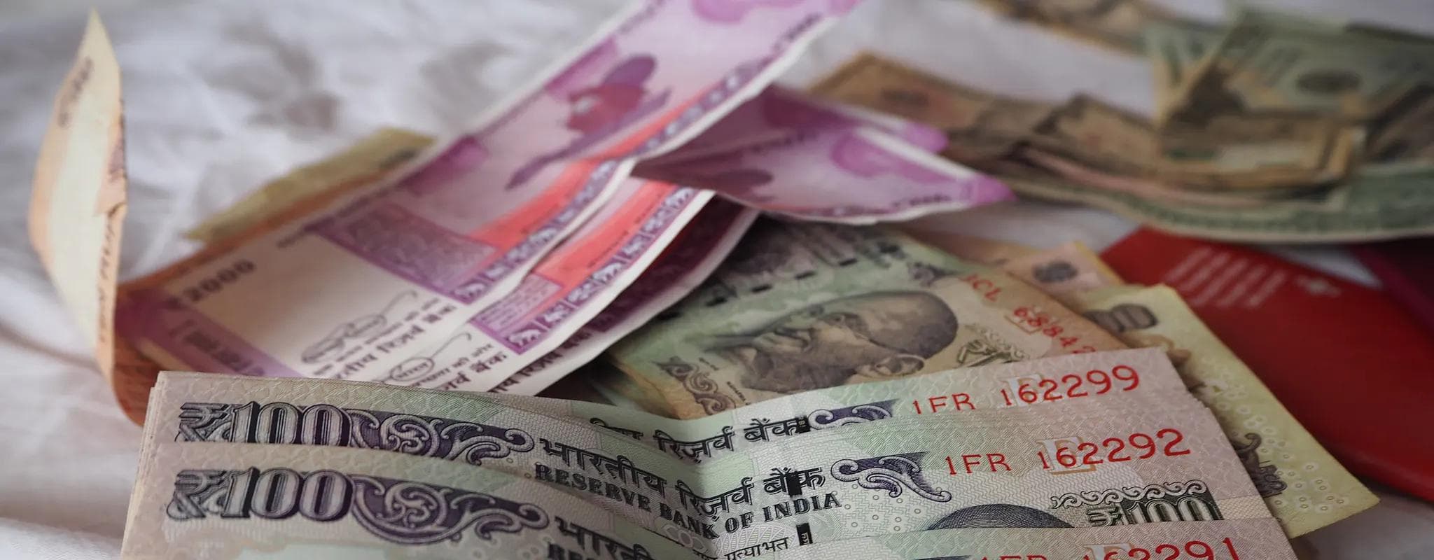 Indian rupee banknotes lie in a shallow stack, with ₹100 notes in the foreground.
