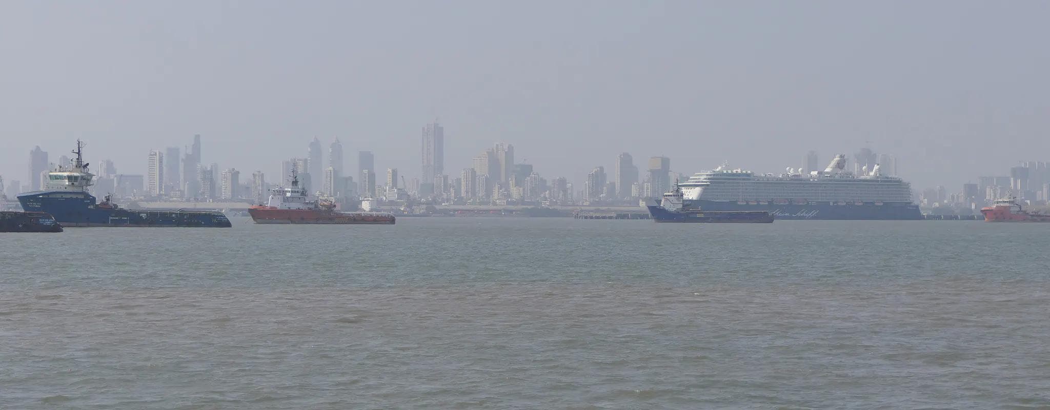 The Mumbai skyline across the harbour with commercial vessels in the foreground.