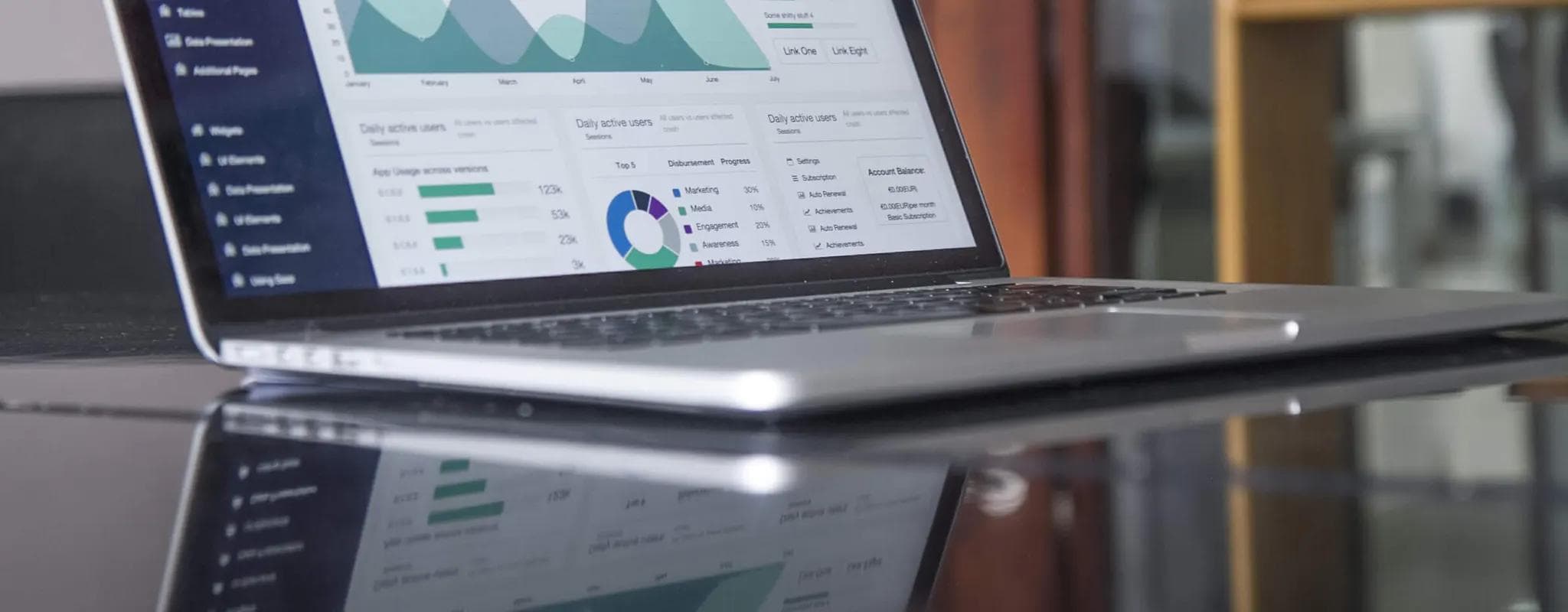 A laptop displays a dashboard of charts and performance statistics on a reflective table.