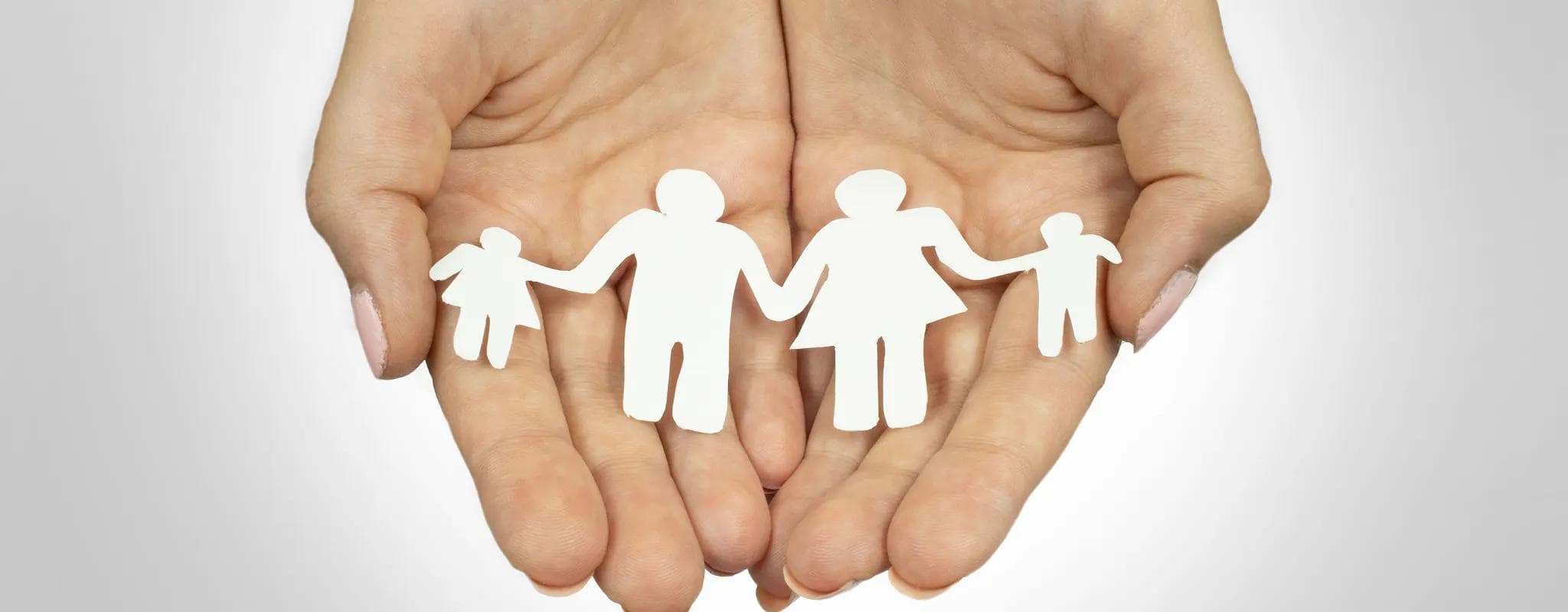 Two open hands hold a white paper cutout of two adults and two children.