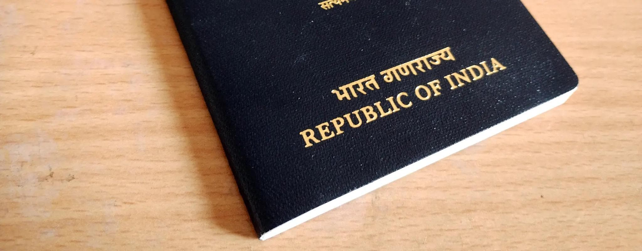 A closed Indian passport rests on a wooden table.